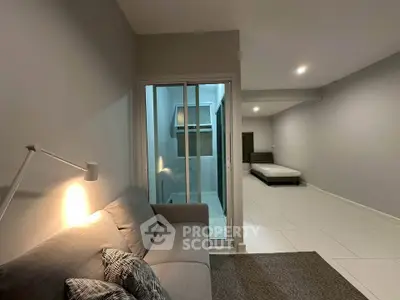 Modern living room with cozy sofa and sliding glass doors leading to a minimalist bedroom.