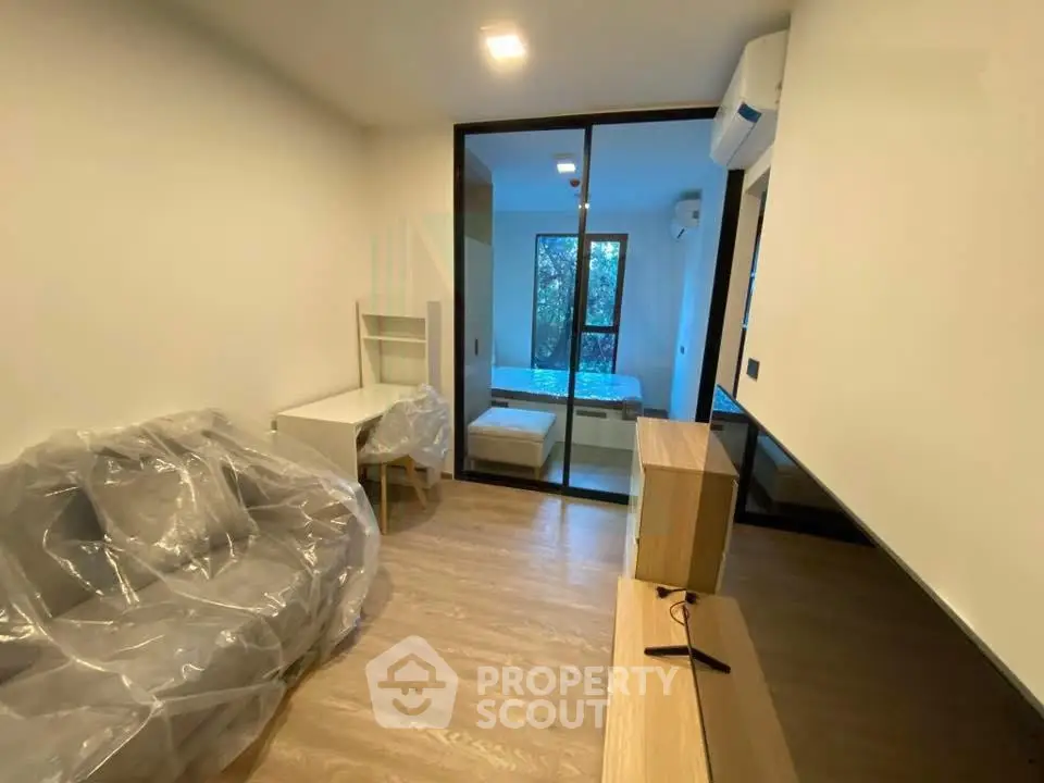 Modern apartment interior with glass partition, featuring a cozy living area and a view of the bedroom.