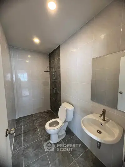 Modern bathroom with sleek fixtures and tiled walls, featuring a toilet, sink, and shower area.