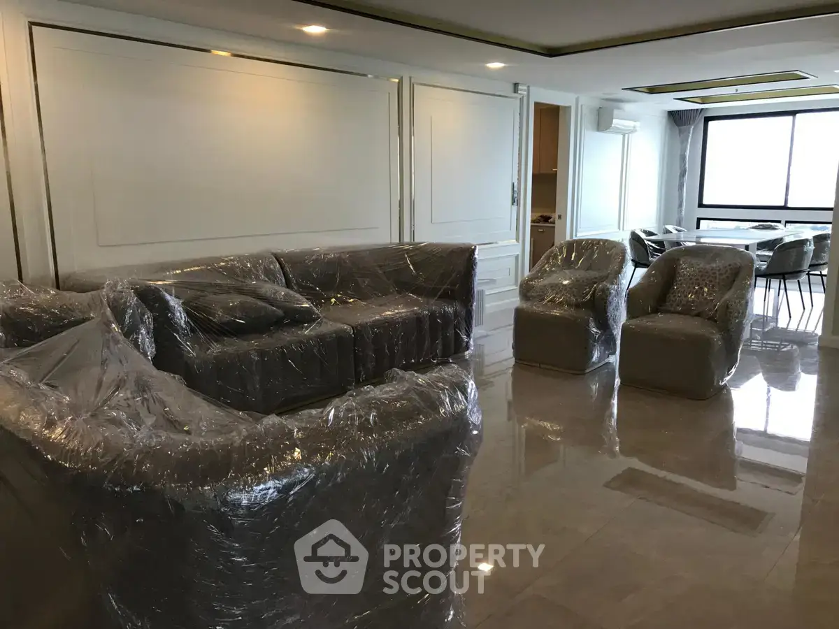 Spacious living room with modern furniture wrapped for protection, featuring large windows and elegant flooring.