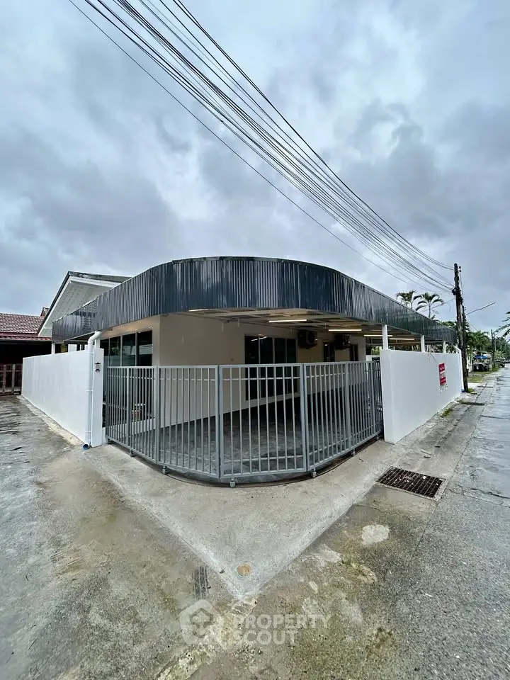 Modern single-story home with sleek design and gated entrance on a cloudy day.