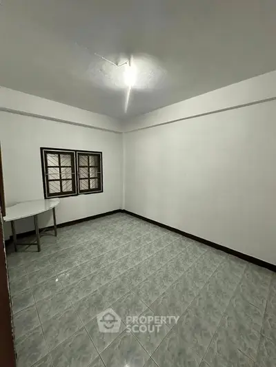 Spacious empty room with tiled flooring and two windows, ideal for customization.