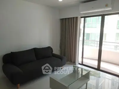 Modern living room with sleek sofa and glass coffee table, featuring a balcony view.