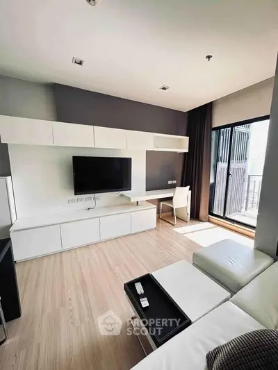 Modern living room with sleek white furniture and large window offering natural light.