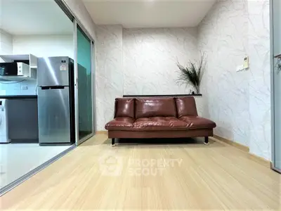 Modern living room with sleek leather sofa and open kitchen layout, featuring stainless steel appliances.