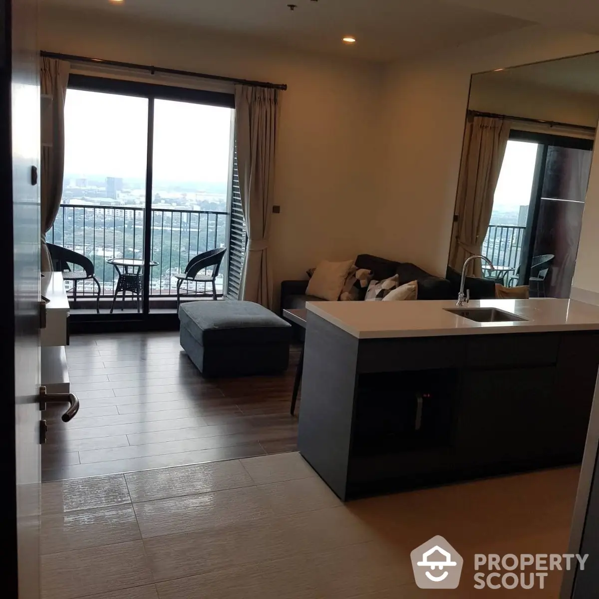 Modern studio apartment with open kitchen layout, large windows leading to a cozy balcony with a view, and a comfortable living area.