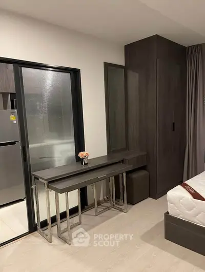 Modern bedroom with sleek furniture and sliding glass door leading to kitchen area.