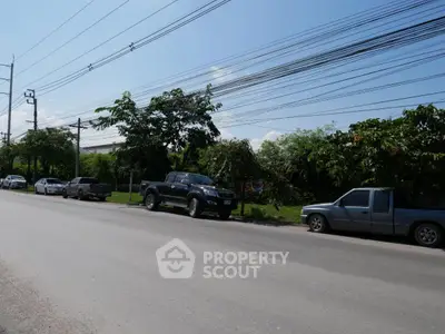 Spacious roadside view with greenery and parked cars, ideal for urban development.