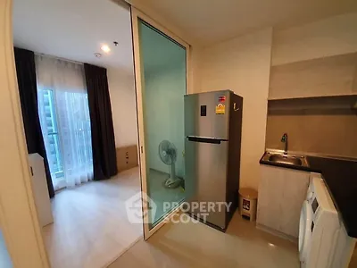 Modern apartment kitchen with stainless steel fridge and washing machine, adjacent to a bright living area.
