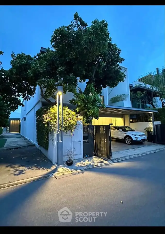 Modern two-story house with carport and lush greenery in a serene neighborhood.