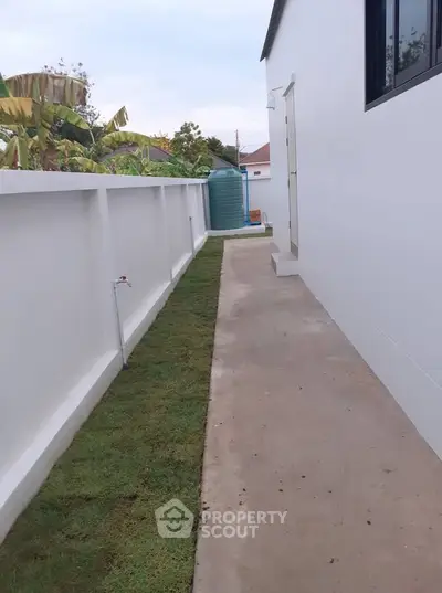 Modern side pathway with fresh grass and white walls leading to backyard