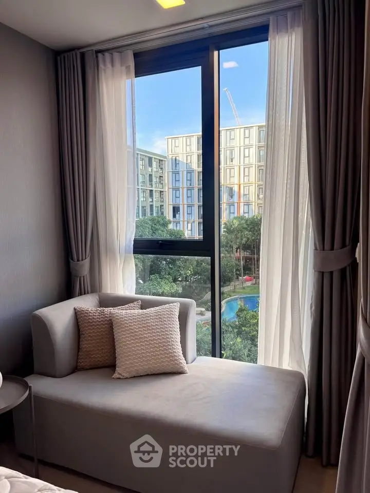 Modern living room with large window offering stunning city view and cozy seating area.