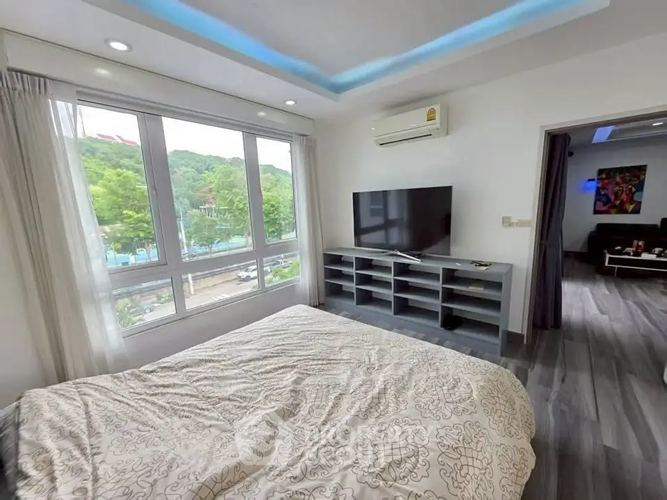 Modern bedroom with large window and scenic view, featuring a TV and stylish decor.