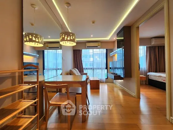 Modern open-plan living room with dining area and bedroom view, featuring stylish lighting and wooden flooring.