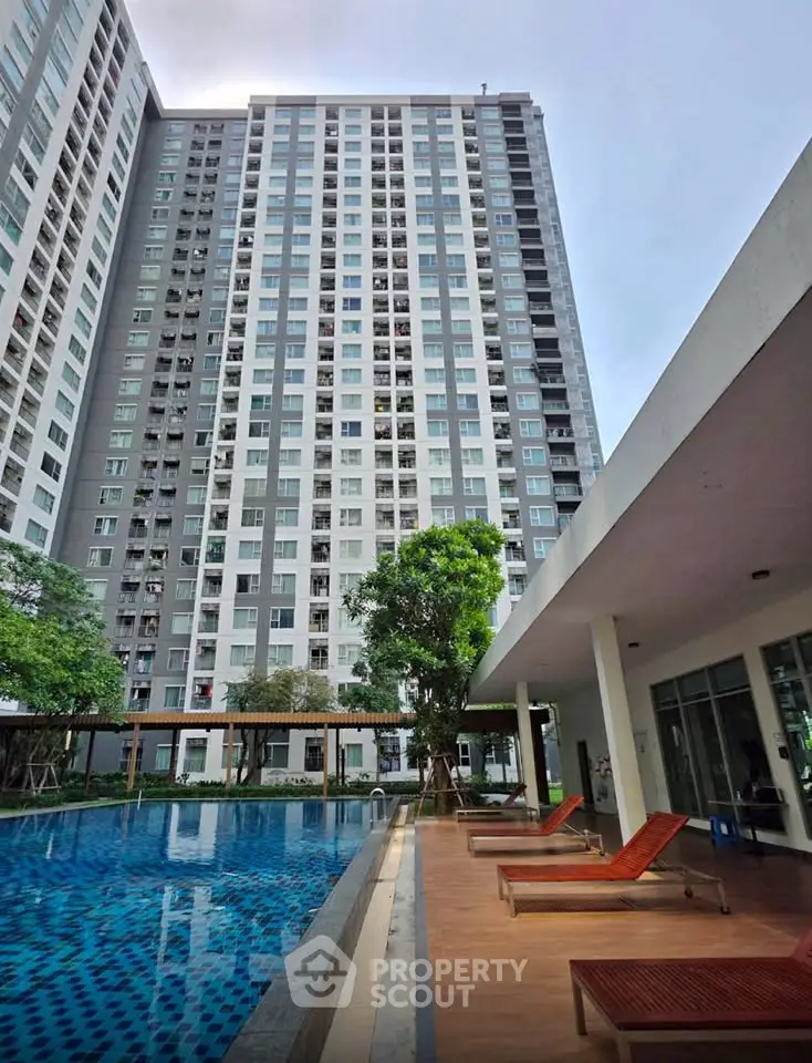 Modern high-rise building with luxurious poolside area and sun loungers, perfect for urban living.