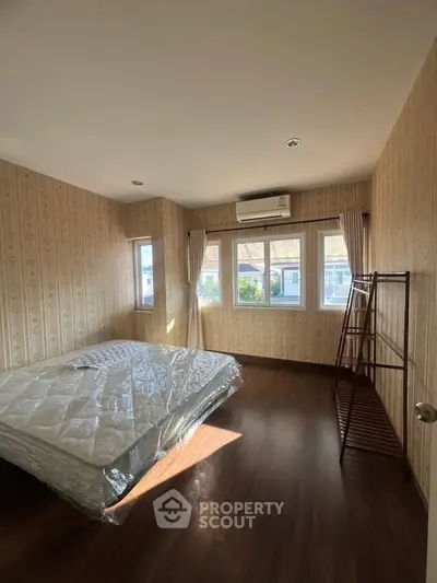 Spacious bedroom with natural light, wooden flooring, and air conditioning in a modern home.