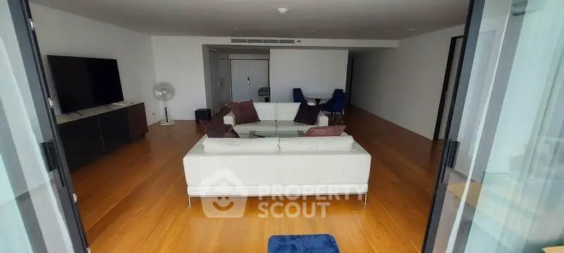 Spacious modern living room with sleek wooden flooring and elegant white sofa set.