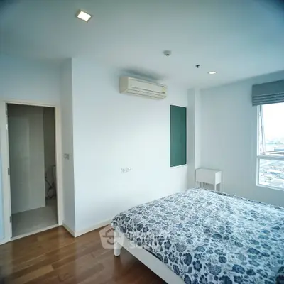 Spacious bedroom with modern decor and city view, featuring wooden flooring and air conditioning.