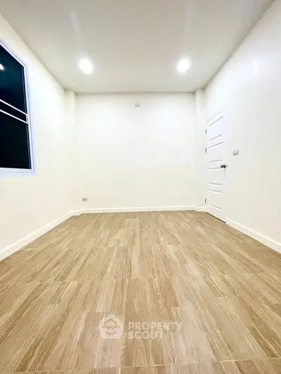 Spacious empty room with wooden flooring and bright lighting, perfect for customization.