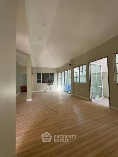 Spacious empty room with wooden flooring and large windows, ideal for customization.