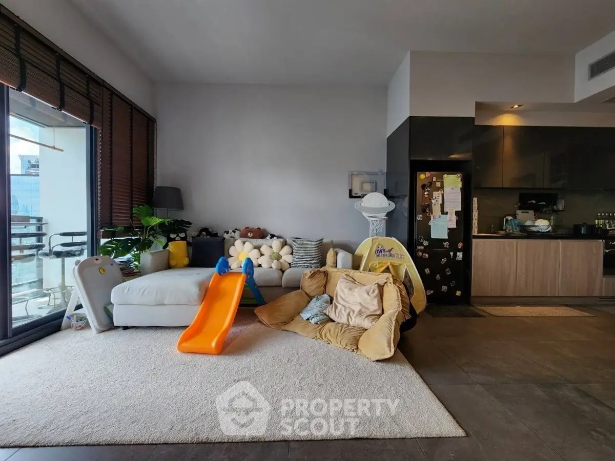 Spacious living room with modern kitchen and cozy play area, featuring large windows and stylish decor.