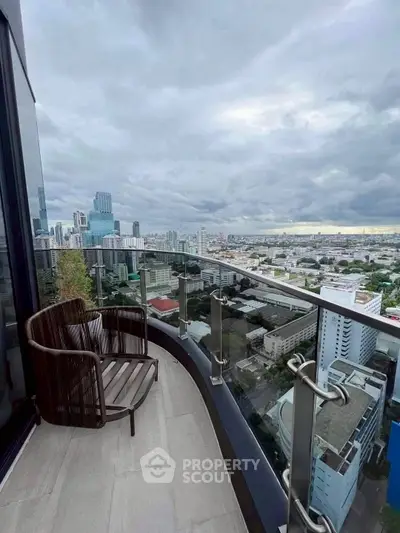 Stunning cityscape view from a modern balcony with glass railing and stylish chair.