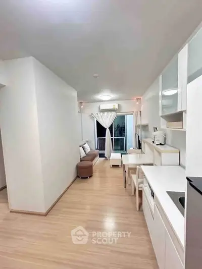 Modern open-plan living room with sleek white cabinetry and cozy seating area, leading to a balcony.