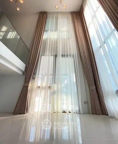 Luxurious high-ceiling living room with elegant floor-to-ceiling curtains and modern lighting.