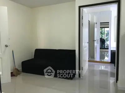 Modern living room with sleek black sofa and glossy tiled floor, leading to a bright hallway.