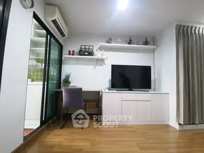 Modern living room with TV, desk, and sliding glass door to kitchen.