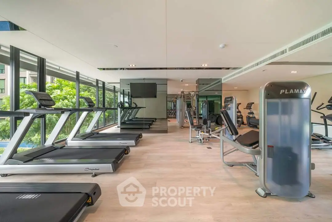 Modern gym with state-of-the-art equipment and large windows offering a lush green view.