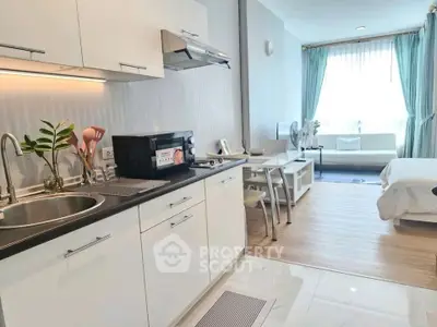 Modern studio apartment with open kitchen and cozy living area, featuring sleek white cabinetry and natural light.