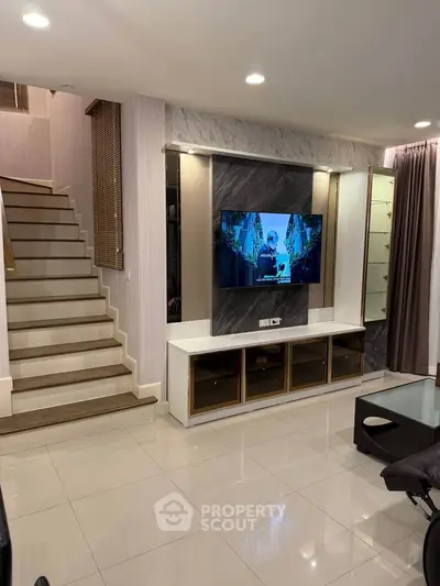 Modern living room with sleek staircase and mounted TV, featuring elegant decor and ample lighting.