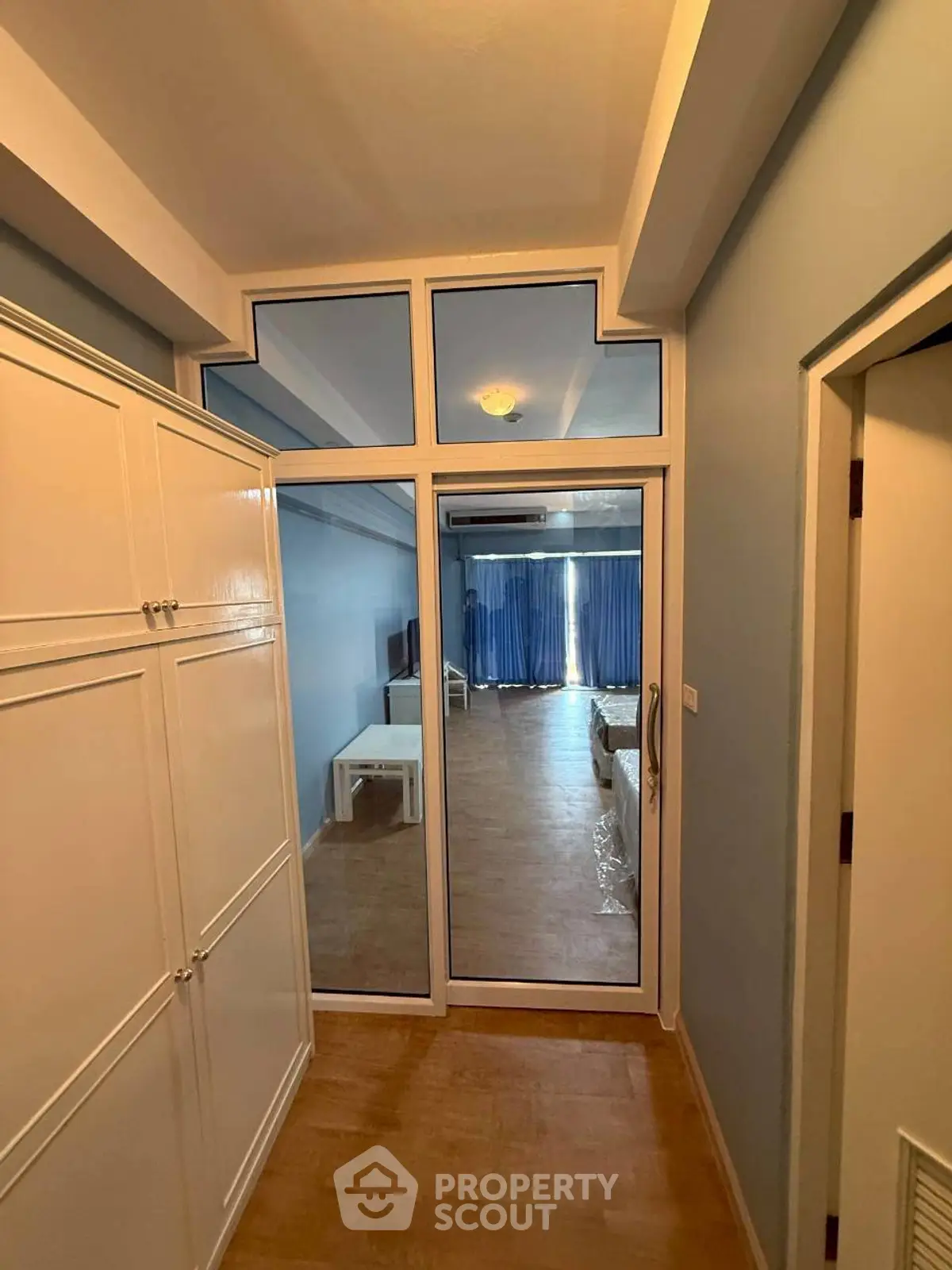 Spacious apartment hallway leading to a bright living room with large windows and blue curtains.