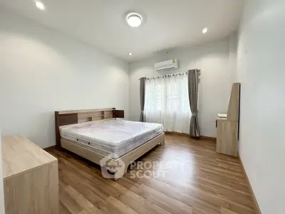 Spacious bedroom with wooden flooring and natural light, featuring a comfortable bed and modern air conditioning.