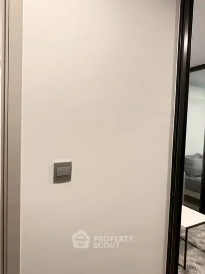 Minimalist interior wall with modern light switch and glimpse of a cozy living area.