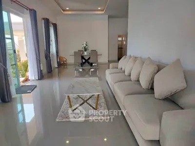 Spacious modern living room with elegant sofa and dining area, featuring large windows and glossy flooring.