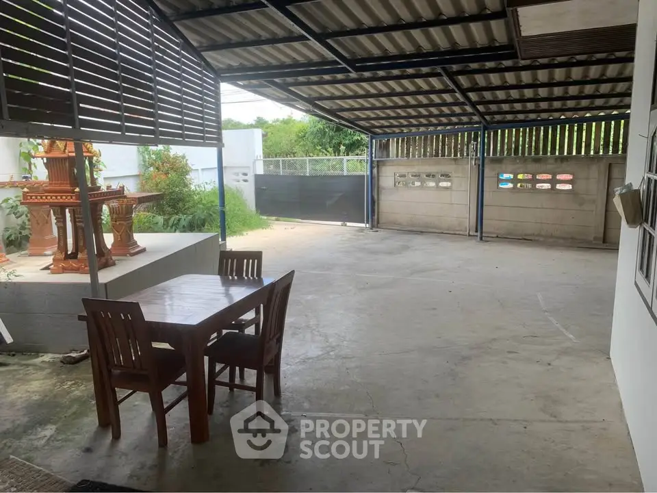 Spacious covered outdoor area with dining set and garden view, perfect for relaxation and gatherings.