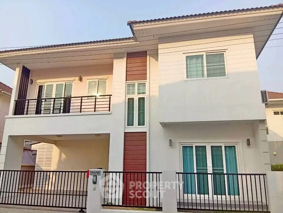 Modern two-story house with balcony and gated entrance, featuring sleek design and large windows.