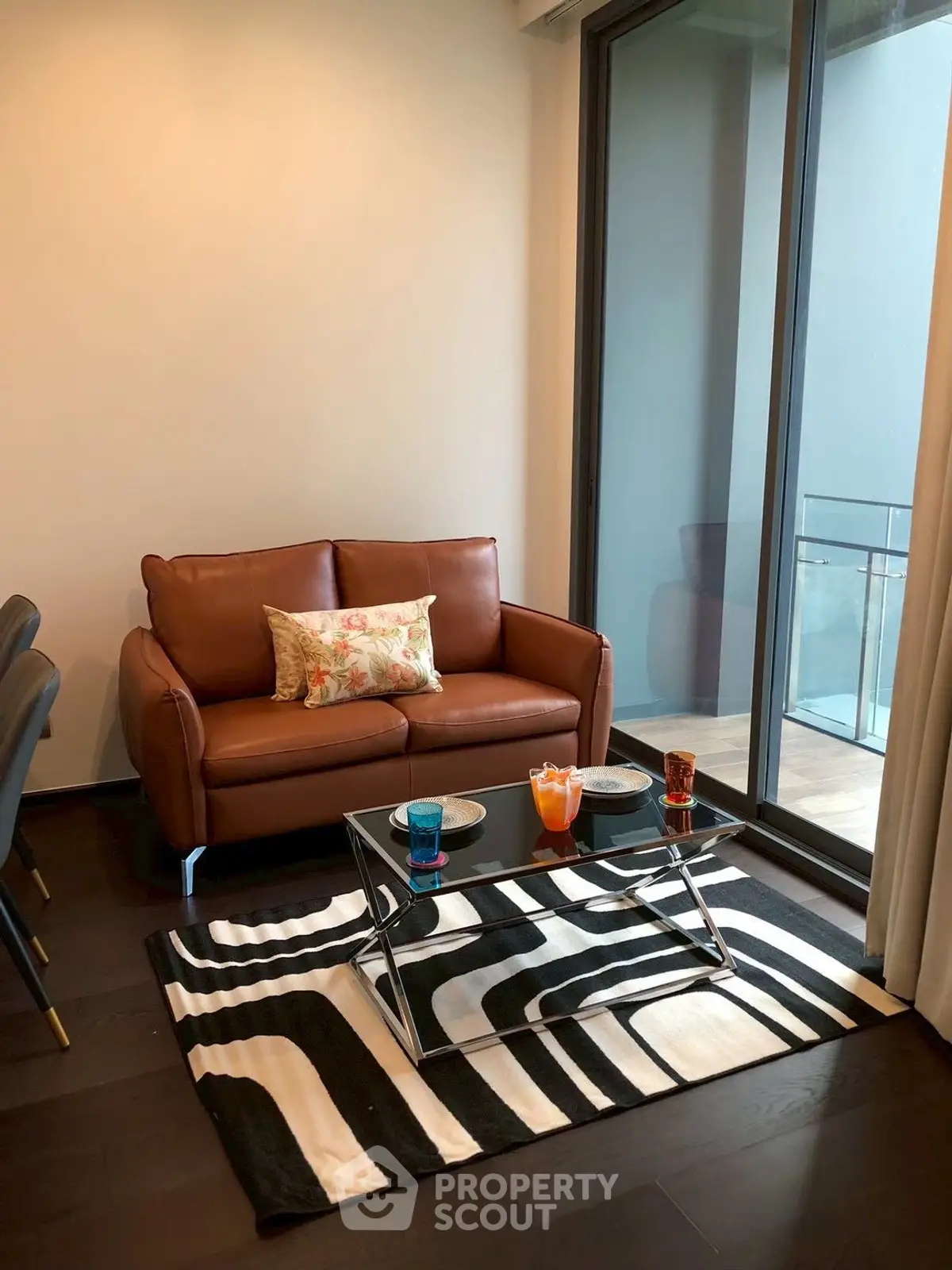 Stylish living room with leather sofa and glass coffee table, featuring a modern rug and balcony view.