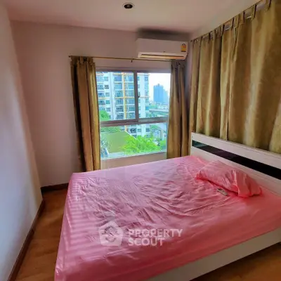 Cozy bedroom with pink bedding and large window offering city view in modern apartment.