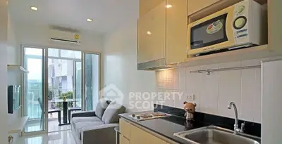 Modern compact kitchen with open layout and cozy living area leading to a balcony with natural light.