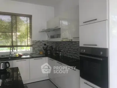Modern kitchen with sleek white cabinets and built-in oven, featuring a stylish backsplash and natural light.