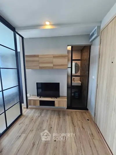 Modern living room with wooden flooring and sleek TV unit adjacent to a compact bathroom.