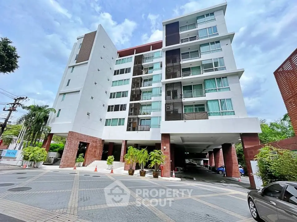 Modern multi-story residential building with spacious parking area and lush greenery.