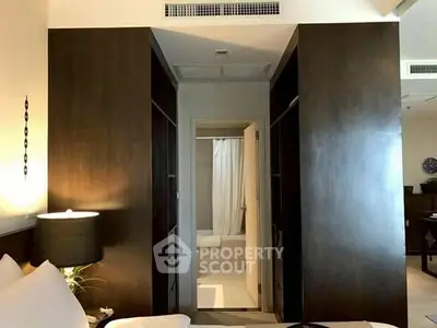 Modern bedroom with ensuite bathroom featuring sleek dark wood cabinetry and ambient lighting.