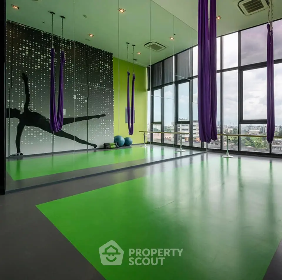 Modern gym with aerial yoga setup and city view, featuring vibrant green flooring and mirrored walls.