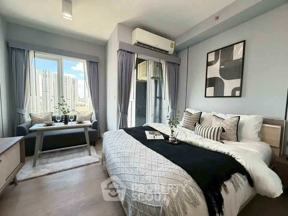 Modern bedroom with city view, stylish decor, and cozy seating area.