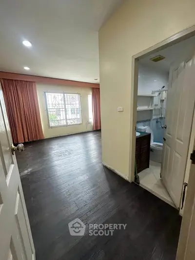 Spacious living area with dark wood flooring and adjacent bathroom, featuring large window for natural light.