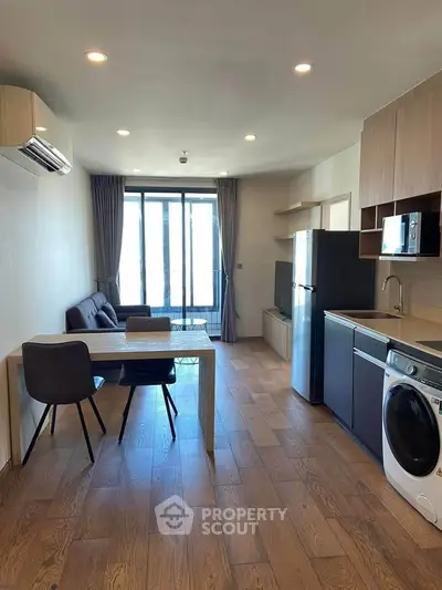Modern open-plan living room with kitchen, featuring wooden floors and natural light.